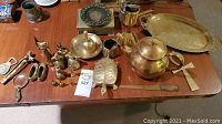 Full view of brass tea pot, tray, turtle, cat figurine, and various other brass decorative items on wooden table.