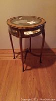 Front view of small round display table showing beveled glass top and slender cabriole legs.