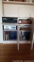 Overview of stereo equipment setup inside cabinet showing the turntable on top shelf, cassette player below, and vinyl records in compartments