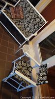 Folding love seat and chair with black and white floral and geometric pattern fabric on white wooden frames, showing folding patio furniture setup indoors on brown tiled floor.