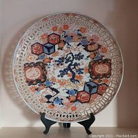 Front view of 24.5-inch round porcelain charger with Imari-style decoration on black display stand