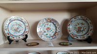 Three Imari ware plates with hand-painted floral and geometric designs displayed on stands