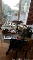 Wide view of multiple kitchen items on table including coffee makers, flatware, bowls, plates, and a small vase