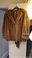Full front view of mid-length brown mink fur coat hanging on black hanger