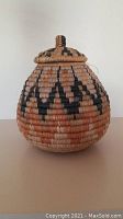 Front view of the Coast Salish woven basket with lid, showing the bulbous shape and black geometric pattern on natural fibers.