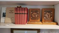 Books with red covers including Ogden Nash titles, history books in background, and wooden trophies side by side on shelf