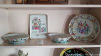 Four ceramic dishes displayed on shelf: two oval shallow bowls, a rectangular tray, and a round plate