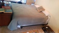 Full view of queen bed made with quilt coverlet and pillows, showing frame and bedding.