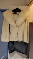 Full view of white rabbit fur coat with thick collar on hanger