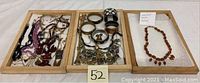 Wide view of two wooden trays showing assorted bracelets, necklaces, earrings, and a separate tray holding the vintage Baltic amber necklace on bubble wrap.