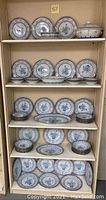 Full view of wooden shelving unit with multiple shelves containing the entire blue and white porcelain dinnerware set including plates, platters, bowls, and covered casserole.