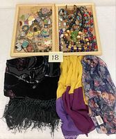 Photo showing two wooden trays filled with assorted costume jewelry plus three scarves laid beneath them.