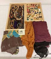 Lot showing assorted beaded and wooden bracelets in one tray, assorted costume earrings in another tray, and four scarves laid out flat next to trays.