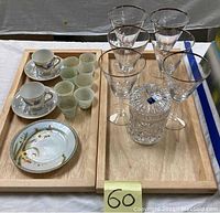 Overview of lot items on wooden trays: 4 etched martini glasses, 4 demitasse cups with saucers, 5 jadeite saki cups, lidded crystal jar