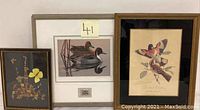 Three framed prints grouped together on a white wall showing bird, duck, and butterfly-themed artwork.