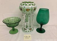 Three glass pieces shown together: green footed bowl on left, decorative white and green vase with crystal prisms center, green goblet on right.