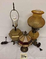 Full view of three lamps with electrical cords visible. Included are amber hobnail lamp, slag glass panel lamp, and porcelain base lamp.