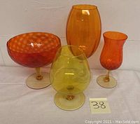 Four vintage retro colored glass pieces including orange and yellow stemmed glasses and a comport.