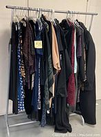 Wide view of the entire clothing rack showing a collection of jackets, sweaters, tops, coats, and dresses in dark colors and various patterns.