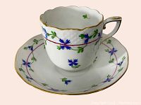 Teacup and saucer set shown from an angled side view to display floral decoration and gold trim.