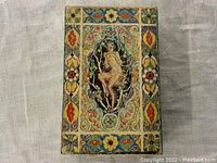 Front view of the antique paper pan box showing colorful floral and geometric painted design with a central image of a seated figure.