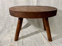 Front angle view of round wooden foot stool showing top and all three legs.