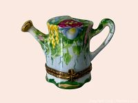 Front and side view of the hand-painted Limoges porcelain watering can pill box showing floral design and spout.
