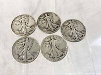 Obverse side of five Walking Liberty half dollar coins, showing Lady Liberty with sun and 'In God We Trust' text