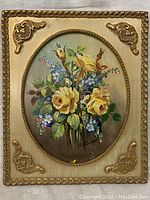 Full view of oil painting of floral arrangement framed in ornate gold-colored frame with decorative corner accents.