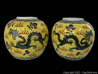 Pair of yellow antique ginger jars side by side on black background showing full decoration and shape