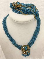 Necklace displayed on a bust showing blue glass beads and decorative clasp with rhinestones.