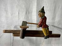 Side profile of the hand-carved man holding an axe mid-chop, attached to a wooden base with a log section.