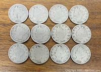 Photo showing 12 Liberty Head Nickels arranged in three rows of four on a wood surface, displaying various dates from 1899 to 1912 and varying wear conditions.