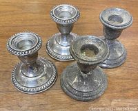 Four weighted silver candlesticks showing contrasting condition: two more polished and two heavily tarnished, all with a rope edge design on base and candle holder lip.