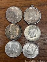Top view of six 1964 Kennedy Half Dollar coins laid out on wood surface showing obverse side with John F. Kennedy profile; one coin attached in a medallion holder.