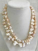 Pair of cultured pearl necklaces displayed on white necklace bust, showing irregular baroque pearls in cream and peach hues doubled in layers.