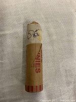 Photo of a single roll of 1956 wheat pennies in original paper coin wrapper marked with '56' and '50 pennies' text visible.