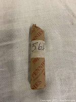 Full view of a single roll of unsearched 1956 D wheat pennies, wrapped in original penny roll paper with '561' written on white tape.