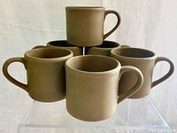 Set of six brown stoneware mugs arranged on clear acrylic stand showing front and side views