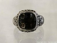 Front view showing faceted cushion-cut smoky gray gemstone set in ornate sterling silver filigree ring band.