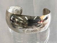Front-facing image of polished sterling silver wide bangle bracelet with reflective surface.