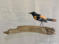 Side view of the hand painted oriole bird decoy on driftwood base showcasing detailed painting and the bird's legs attached to the wood.