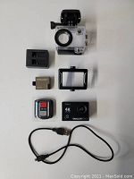 Dragon Touch Vision 3 action camera with battery, remote, waterproof case, mounting frame, and USB charging cable laid out on white surface.