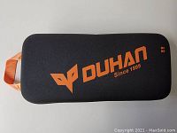 Closed black hard carrying case with orange Duhan logo on top and orange carrying strap on the side.