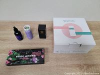 Diffuser and essential oils arranged on wooden surface, with diffuser box, oils in various branded bottles and boxes