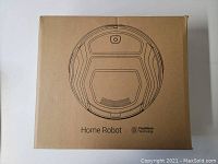 Closed cardboard box with line drawing of a round robot vacuum and label "Home Robot" with FreeMove Technology.