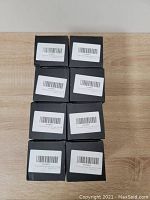 Top view of 8 individual boxed black ashtrays stacked in two columns of four on a wooden surface