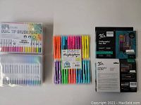 Photo of four Boiros 36-color dual tip brush pen sets, one set of 30 assorted color highlighters, and two Mont Marte calligraphy pen kits with boxes visible.