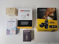 Overview of lot including Dogtra 280C dog trainer box, professional hair clipper box, PET NAIL GRINDER box, ultrasonic bark control device box, and smart bark control collar box.