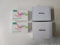 Two sealed Coniler Hearing Amplifier boxes and two sealed white Ushining phone boxes